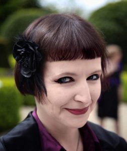 Woman with a complex black flower in her hair smiles into the camera.